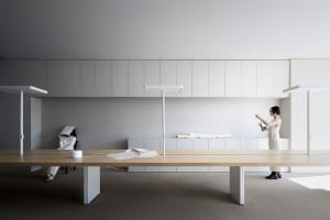 A modern office space featuring a minimalist desk with a light wooden surface and white elements in the background.