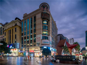 A bustling city center at night with illuminated storefronts and pedestrians walking.