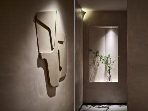 Minimalist interior design featuring textured concrete walls with geometric wall sculptures and a vase with greenery.