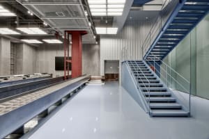 Modern office space with conveyor system, metal stairs, and concrete walls.