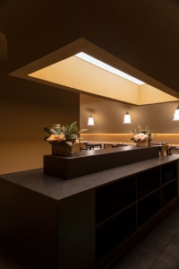 A sleek, dark marble restaurant bar counter with decorative floral arrangements, under illuminated ceiling lighting.