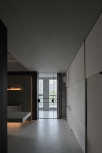 An industrial-style corridor with concrete walls and floor, featuring a sleek, minimalist design with a glass door at the end