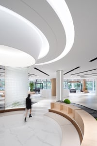 Modern office lobby featuring a white marble floor, glass walls, and wood accents