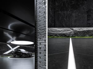 A sleek, minimalist showroom interior featuring a black vehicle displayed on a circular platform with lighting and black mate
