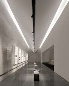 A spacious museum exhibition hall with polished concrete floors and minimalist exhibits.