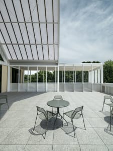 Outdoor seating area with concrete table and metal chairs under a metal roof structure.