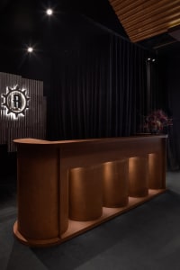 A contemporary, industrial-style reception desk crafted from copper, featuring sleek, cylindrical columns illuminated by warm