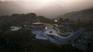 A modern, curving concrete building with a green roof set against a mountainous landscape.