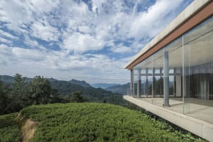 A modern residential terrace with glass walls overlooking green fields and mountains.