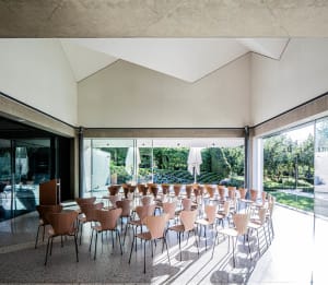 A modern conference room featuring glass walls, concrete ceiling, and wooden chairs arranged in a semi-circular fashion.