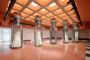 Modern exhibit space featuring glass and metal displays and white dresses.