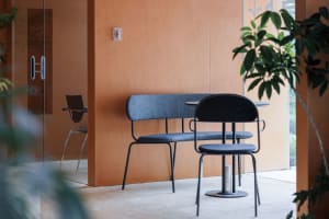 A modern interior space featuring a metal bench with a cushioned seat and backrest, next to a small round table with a glass 