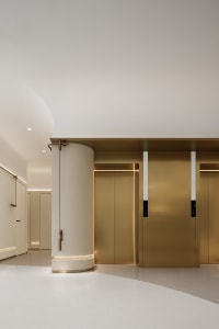 A modern minimalist hotel lobby featuring metallic brass finishes and a cylindrical column.