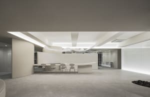 A minimalist office reception space with concrete flooring and a white reception desk.