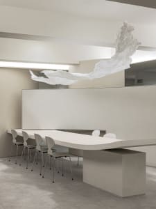 A modern conference room with a minimalist design, featuring a textured concrete table, white chairs, and a floating white pa