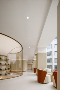 A modern interior corridor featuring white walls, glass walls, bronze accents, and concrete flooring.