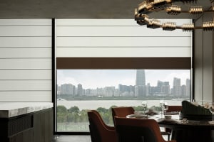 A modern minimalist dining room with a round table, red chairs, a chandelier, and a view of the city skyline.