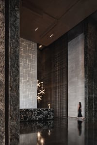 A spacious modern minimalist lobby with marble walls and floors, featuring geometric lighting fixtures and a sleek black rece