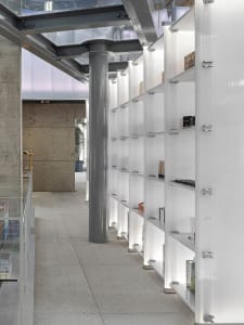 Modern shop interior showcasing white shelves against concrete pillars and a glass ceiling.
