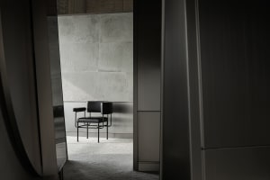 A modern interior with a concrete wall and a single black chair.
