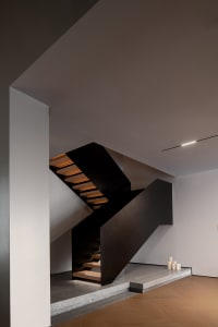 Modern staircase with black handrail and wooden steps illuminated by soft lighting.