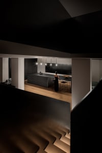 A modern black kitchen interior with a minimalistic design, featuring a long kitchen island with pendant lights and a person 