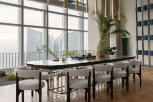 Modern dining room with a large glass table surrounded by chairs, featuring a urban skyline view through floor-to-ceiling win