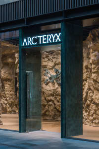 Modern storefront featuring a glass entrance and stone walls with the Arc'teryx logo illuminated.