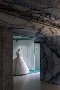 A display of a wedding dress within a room featuring marble and concrete architectural elements.