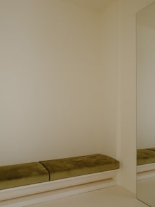 A minimalist interior space featuring a green velvet cushion on a white shelf.
