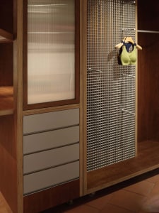 A modern wardrobe with a metal mesh section hanging clothes and a wooden section with drawers and shelves.
