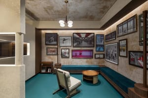 An image depicting a minimalist hotel lobby with concrete walls, wooden furniture, and turquoise accents.