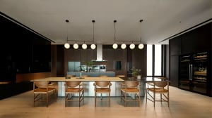 A modern residential kitchen featuring wooden chairs, glass countertops, and stainless steel appliances.