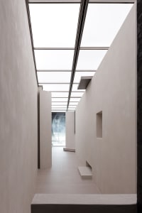 A minimalist corridor with concrete walls and floors, illuminated by a ceiling skylight.