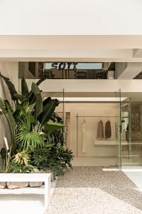 Modern minimalist clothing retail store featuring glass and concrete materials on a tiled floor.