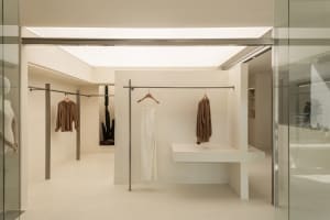 A minimalist retail display featuring neutral colors and clothing on racks and shelves.