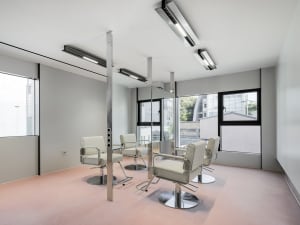 Modern minimalist salon featuring a white metal pole and white chairs against a pink floor.