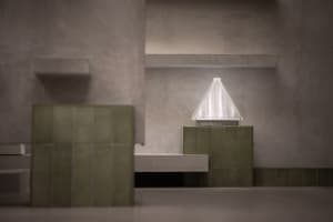 A minimalist interior space with concrete walls and floors, featuring green tiles and a white triangle light fixture.