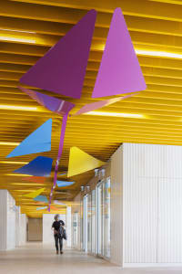 A stylized modern interior corridor with colorful geometric shapes hanging from the ceiling, featuring a geometric metal art 