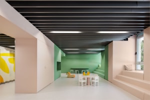 A modern playroom with green walls, white furniture, and colorful toys on the floor. The room features a small table and chai