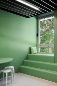 A minimalist green interior with a window seat and stools.