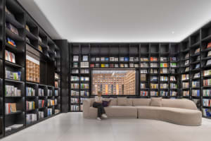 A spacious, industrial-style library with a large, curved sofa and numerous bookshelves filled with books.