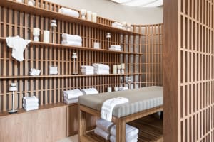 Modern spa treatment room featuring wooden shelves and a massage table with white towels and candles
