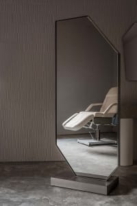 A minimalist floor mirror with a metal frame sits against a textured wall in a modern interior space.