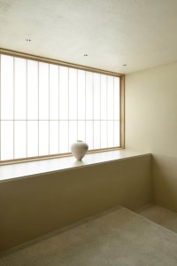 A minimalist indoor space featuring a white ceramic urn on a ledge with a large window.