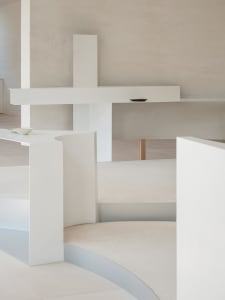 A minimalist interior space with white and concrete elements, featuring a curved staircase and minimal decor.