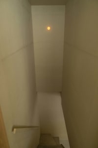 A minimalist staircase made of concrete and glass, illuminated by a singular light source.