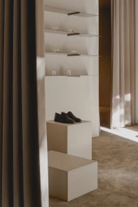 Modern retail store interior with minimalist design, featuring a concrete pedestal displaying a pair of black shoes.