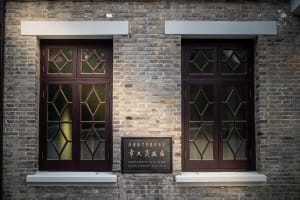 Two brown-framed glass windows with diamond-shaped panes set into a brick wall.