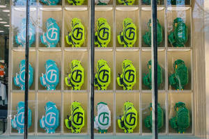 Neon-colored golf bags with the number 6 displayed on them arranged in a grid pattern in a retail display window.